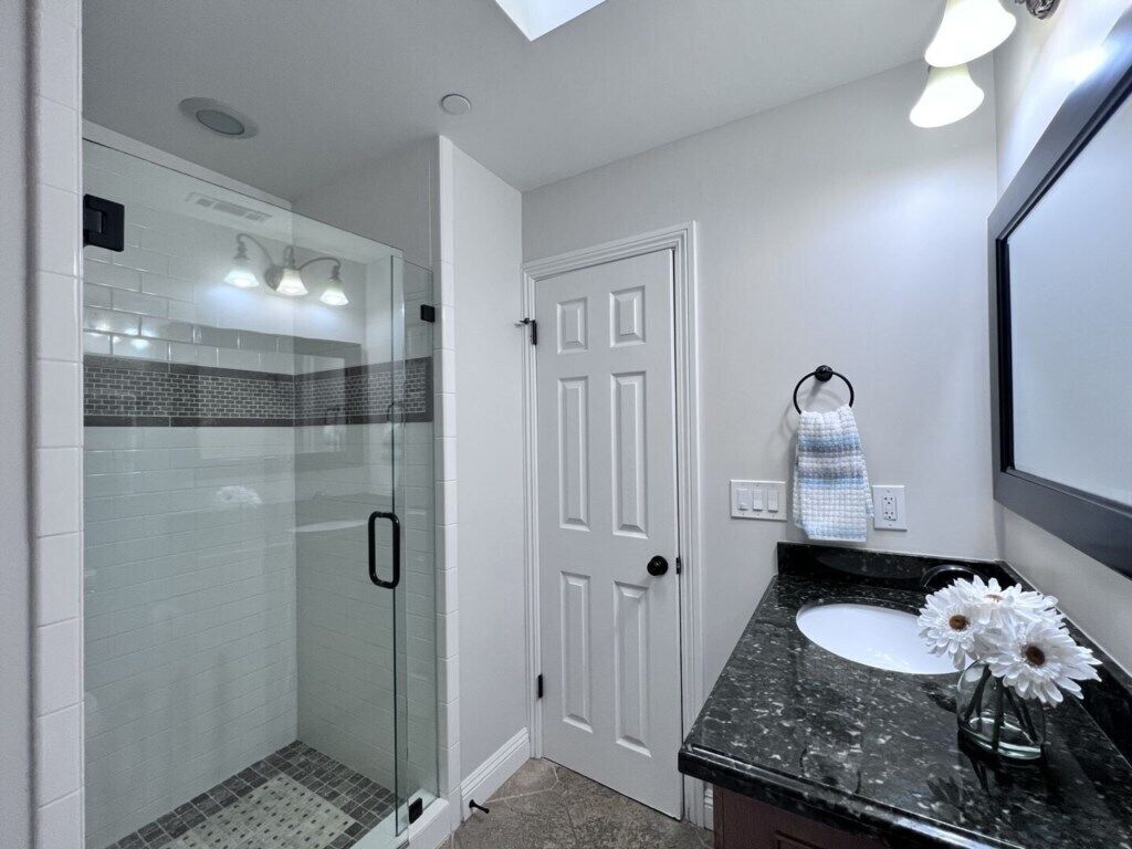 A modern bathroom with a glass shower enclosure, a white door, a marble sink, and a mirror.