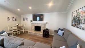 Un salon avec une cheminée, un téléviseur, un canapé, une table à manger avec des chaises et des œuvres d’art accrochées aux murs.
