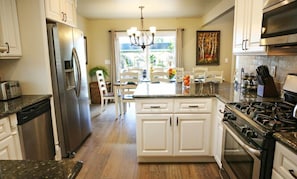 A kitchen with white cabinets, a stainless steel refrigerator, a gas stove, and a dining area with a chandelier.