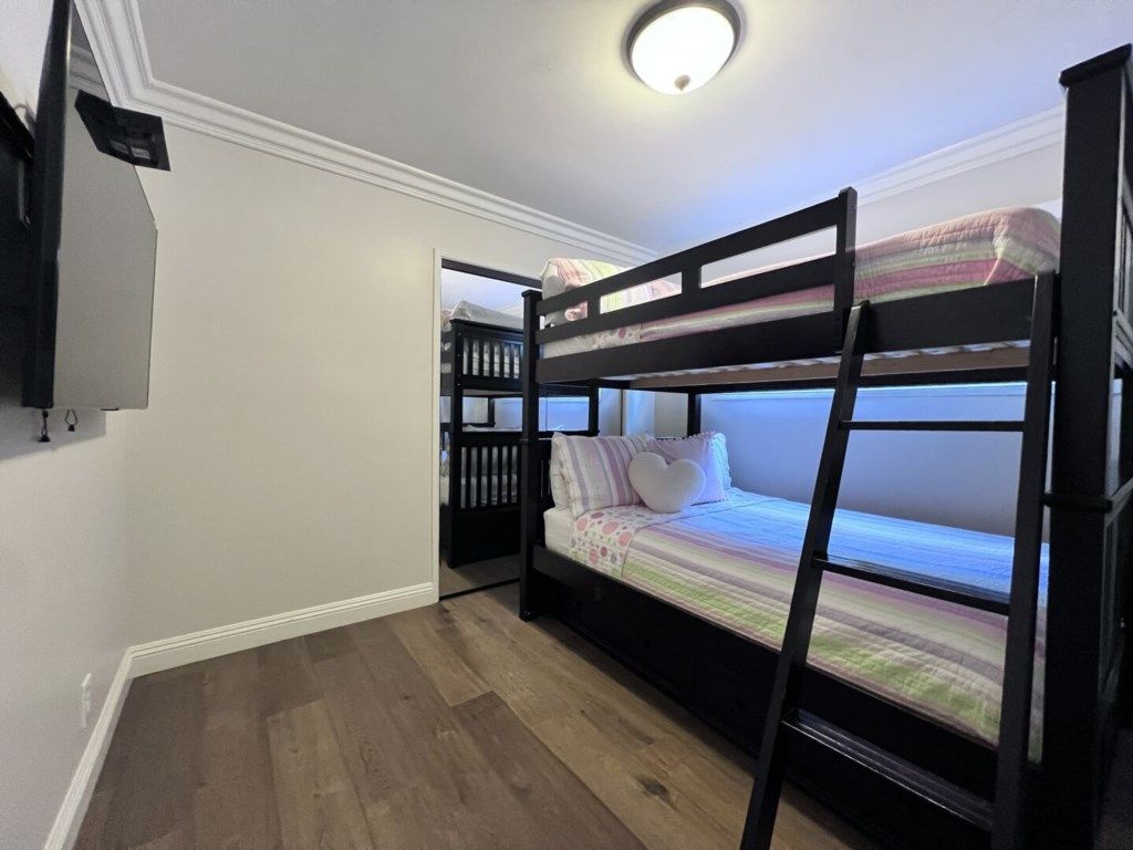 A bunk bed room with a television, a small shelf, and a window.