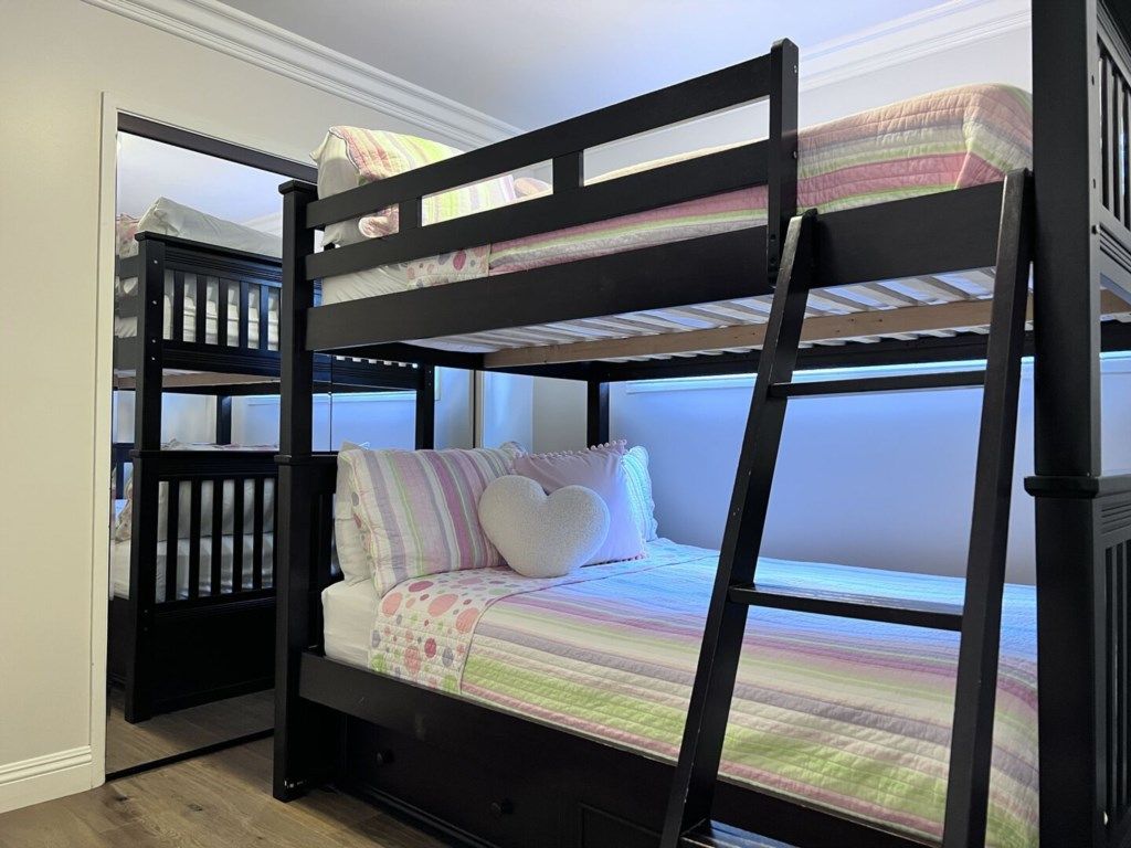 A bunk bed with a striped bedspread and pillows, a window with a view, and a door to another room.