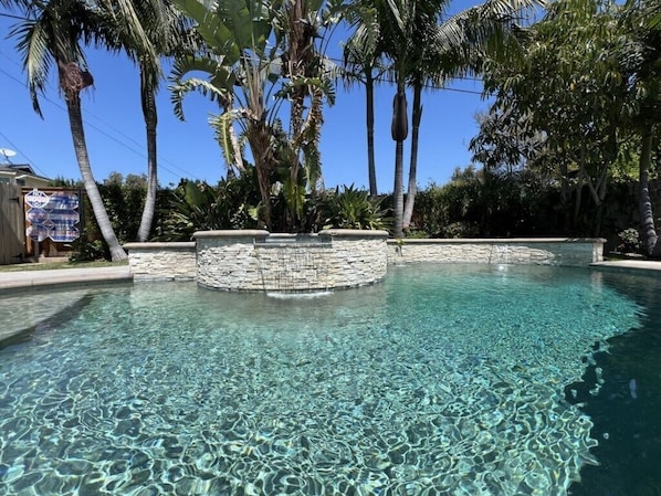 A clear swimming pool surrounded by stone walls and palm trees.
