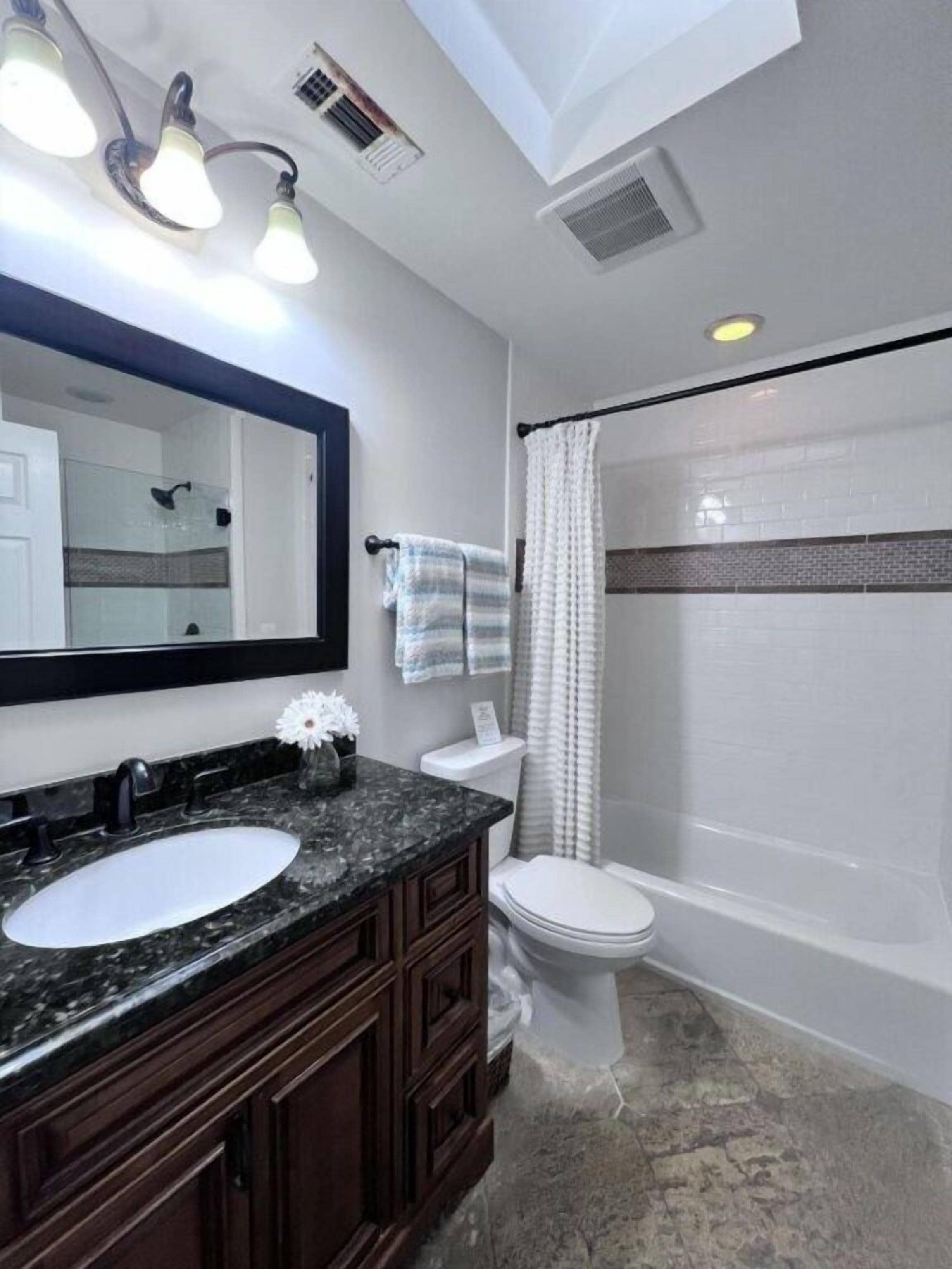 Une salle de bain avec un lavabo en marbre, des toilettes, une baignoire et un rideau de douche.