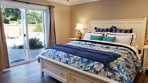 Een slaapkamer met een bed, een nachtkastje, een lamp en een schuifglazen deur die uitkomt op een tuin.