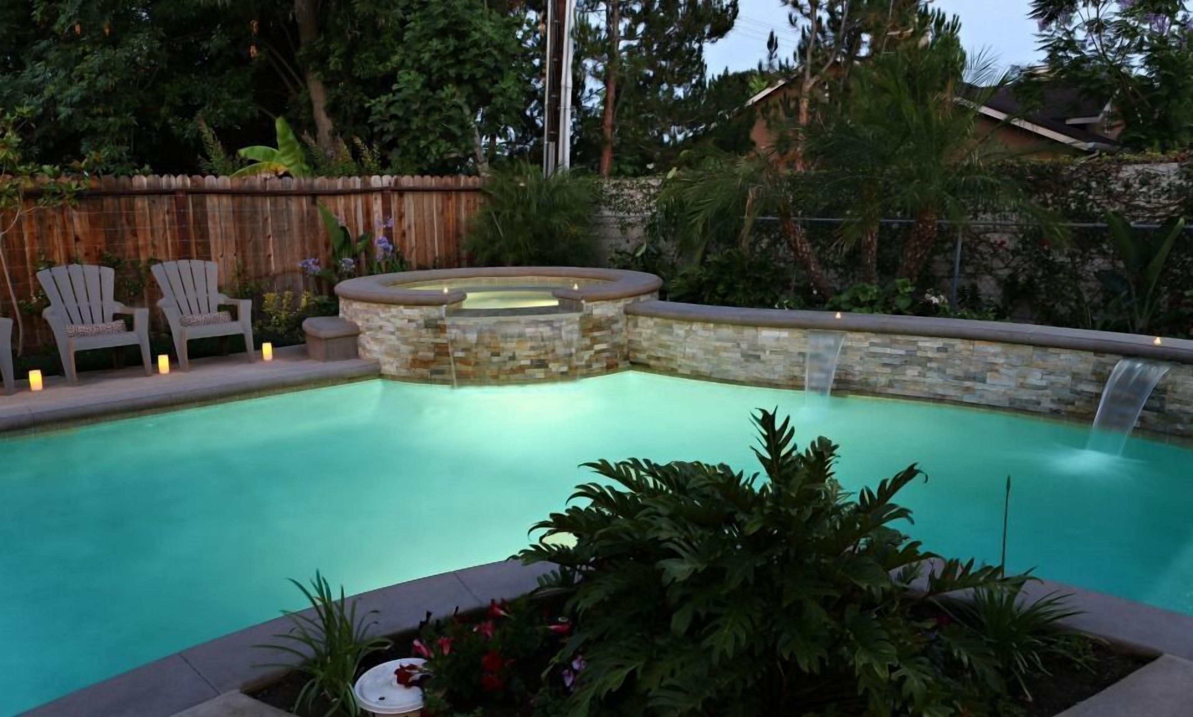 Una piscina con un jacuzzi de piedra, rodeada por una valla de madera y diversas plantas.