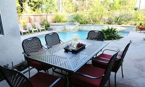 An outdoor patio with a metal table and chairs, a pool, and a wooden fence. - Upscale 6 Bed, 5 Ba, New Pool W/jacuzzi, 1/2 Mile Walk to Disney (Anaheim)