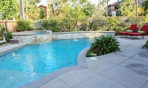 A swimming pool with a stone edge, surrounded by a patio with red chairs and plants.