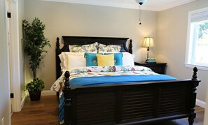 A bedroom with a dark wooden bed, floral bedding, a bedside lamp, and a potted plant. - Upscale 6 Bed, 5 Ba, New Pool W/jacuzzi, 1/2 Mile Walk to Disney (Anaheim)