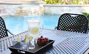 A table with a pitcher of lemonade, glasses, and a bowl of strawberries by a pool. - Upscale 6 Bed, 5 Ba, New Pool W/jacuzzi, 1/2 Mile Walk to Disney (Anaheim)