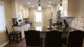 A kitchen with a central island, dark wooden chairs, white cabinets, and a decorative globe. - Upscale 6 Bed, 5 Ba, New Pool W/jacuzzi, 1/2 Mile Walk to Disney (Anaheim)