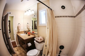 A bathroom with a toilet, sink, mirror, shower curtain, and a window.