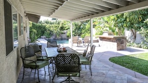 Un patio abrité avec une piscine, des sièges d’extérieur et une végétation luxuriante.