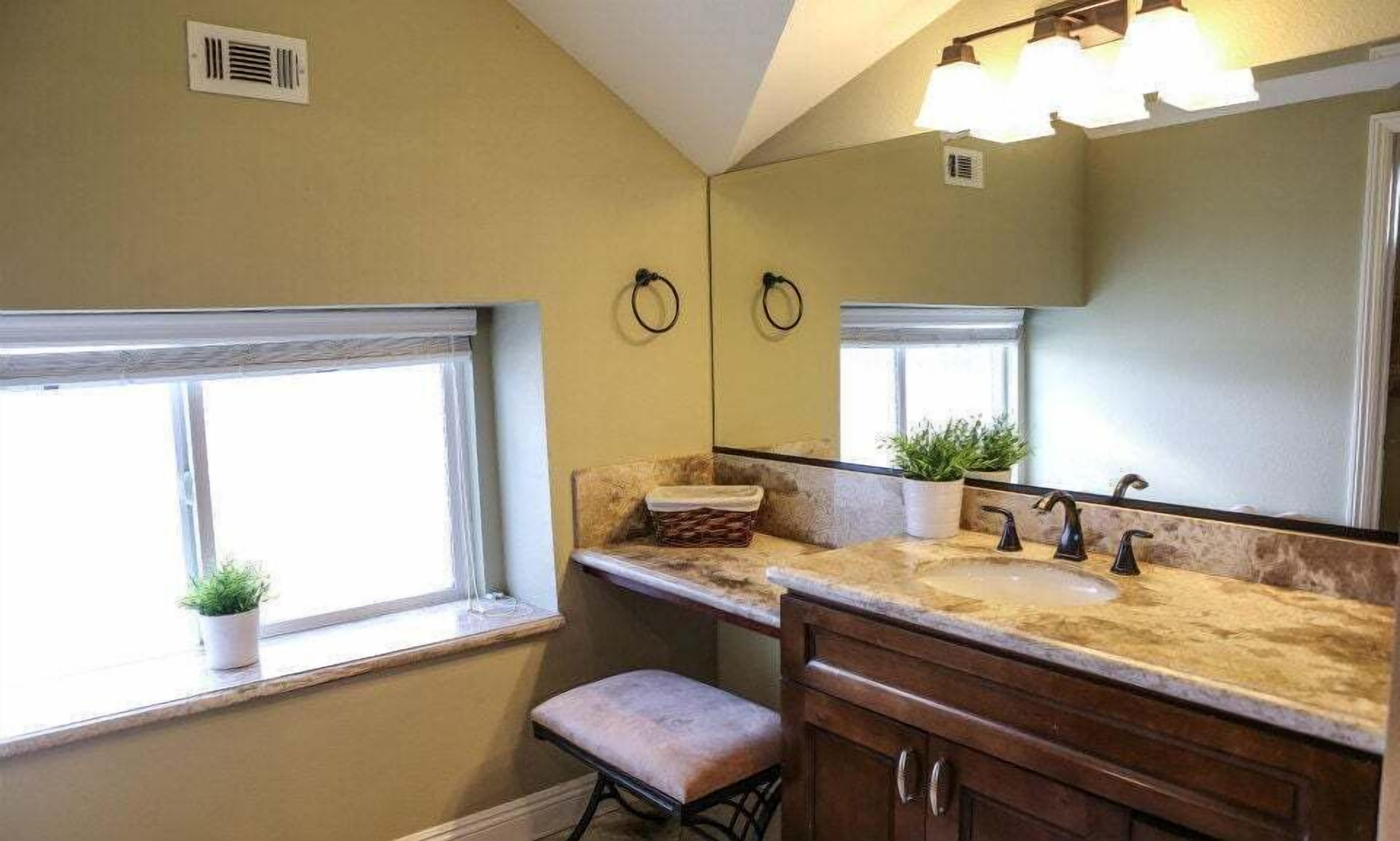A bathroom with two sinks, a large mirror, a window with a plant, and a bench.