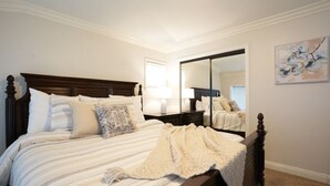 Une chambre à coucher avec un grand lit, une table de chevet, un miroir et un tableau accroché au mur.