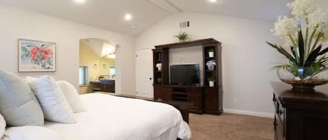 A bedroom with a large bed, a TV, a dresser, and a mirror.