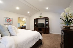 A bedroom with a large bed, a TV, a dresser, and a mirror.