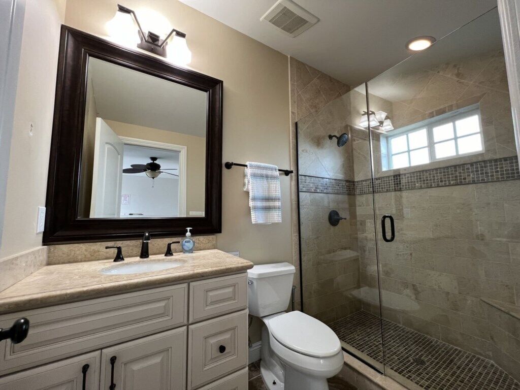A bathroom with a large mirror, a sink, a toilet, and a glass-enclosed shower.