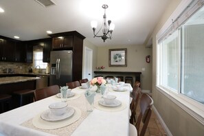A dining area with a long table set for six, a chandelier, and a kitchen in the background. - Highly Upgraded, 5 Bed, 4.5 ba, New Pool W/jacuzzi, 1/2 Mile Walk to Disney (Anaheim)