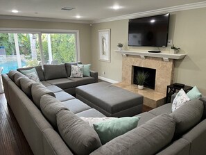 A living room with a sectional sofa, a flat-screen TV, a fireplace, and a view of a swimming pool.