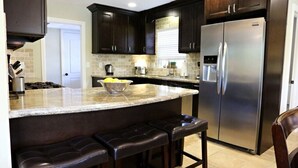 A kitchen with dark wooden cabinets, a stainless steel refrigerator, a granite countertop, and a bowl of lemons. - Highly Upgraded, 5 Bed, 4.5 ba, New Pool W/jacuzzi, 1/2 Mile Walk to Disney (Anaheim)