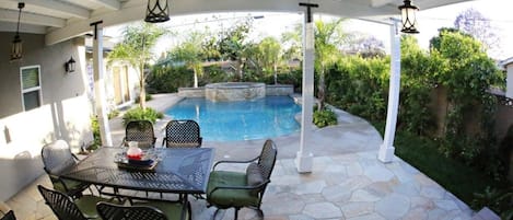 A covered patio with a pool, outdoor furniture, and stone flooring.