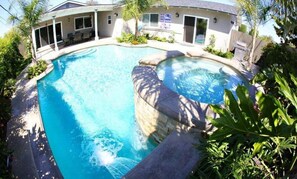A swimming pool with a curved edge, surrounded by a house with a covered patio and a flag.