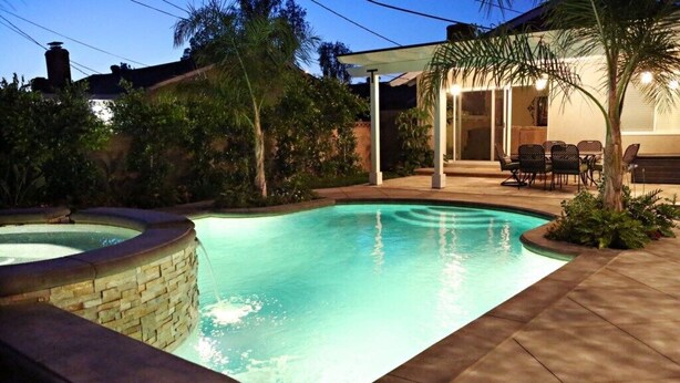 A swimming pool with a stone edge, surrounded by a patio area with chairs and a covered seating area. - Highly Upgraded, 5 Bed, 4.5 ba, New Pool W/jacuzzi, 1/2 Mile Walk to Disney (Anaheim)