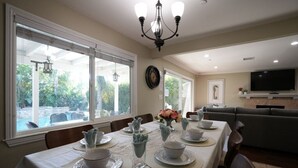 A dining area with a table set for four, a chandelier, a television, and a view of a swimming pool. - Highly Upgraded, 5 Bed, 4.5 ba, New Pool W/jacuzzi, 1/2 Mile Walk to Disney (Anaheim)