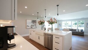 Una cocina moderna con cafetera, armarios blancos e iluminación colgante.