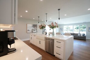 A modern kitchen with a coffee machine, white cabinetry, and pendant lighting. - 4 bedroom, 2 bathrooms (Orange)