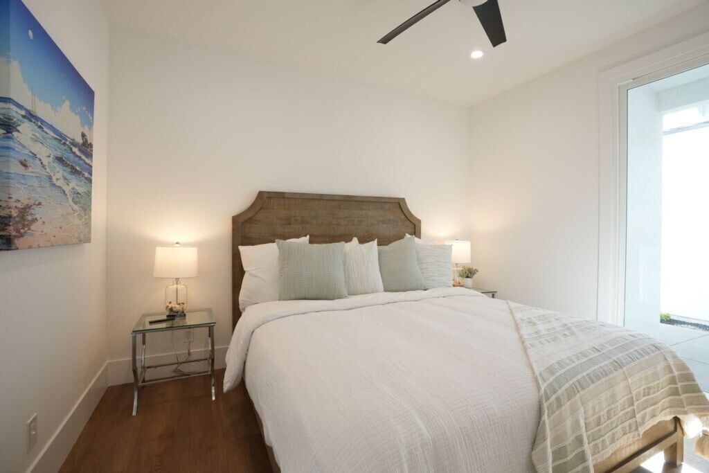 Une chambre avec une tête de lit en bois, un lit recouvert de linge de lit blanc, une table de chevet avec une lampe et un tableau accroché au mur.