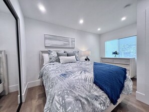Un dormitorio moderno con una cama, una mesita de noche, una lámpara y una ventana con persianas.