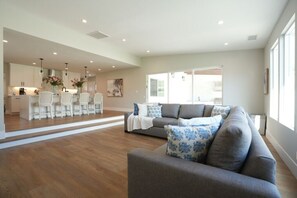 A spacious living area with a grey sofa, white chairs, and a kitchen in the background. - 4 bedroom, 2 bathrooms (Orange)