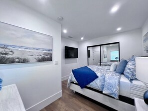 Quarto com uma cama, um quadro, uma televisão e um espelho.