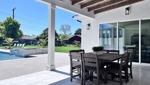 Un patio exterior con una mesa y sillas de comedor, una piscina y una zona cubierta con techo de madera.