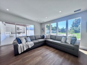 Un salon moderne avec un canapé d’angle, de grandes fenêtres et une vue sur l’extérieur.