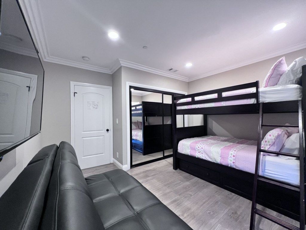 Une pièce avec un lit superposé, un canapé, une porte et un miroir.