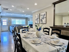 A dining area with a table set for four, a vase with flowers, and a large mirror on the wall.