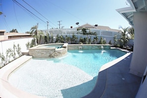 A swimming pool with a stone accent wall, surrounded by a white fence, and a clear blue sky.