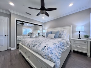 A bedroom with a bed, nightstands, a ceiling fan, and a large mirror.