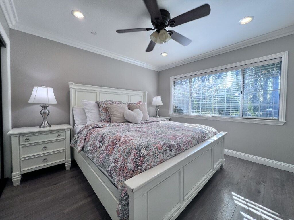 A bedroom with a bed, nightstands, a ceiling fan, and a window with blinds.