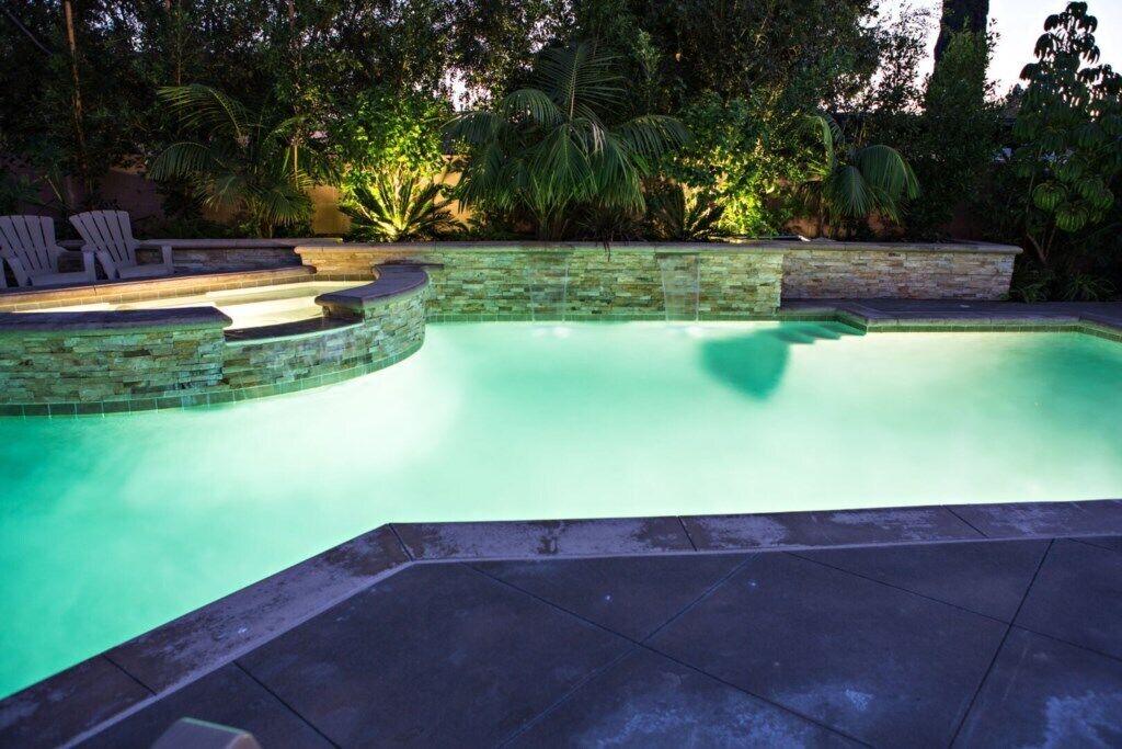 A swimming pool with a stone border, surrounded by greenery and a stone wall.