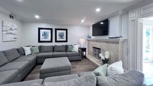 A modern living room with a sectional sofa, a fireplace, and a flat-screen TV mounted on the wall. - Sensational 6 Bedroom 4 Bathroom Pool Home (3 Master Bedrooms W/bathrooms) (Anaheim)
