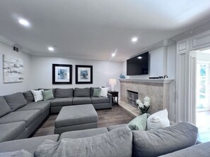 A modern living room with a sectional sofa, a fireplace, and a flat-screen TV mounted on the wall.