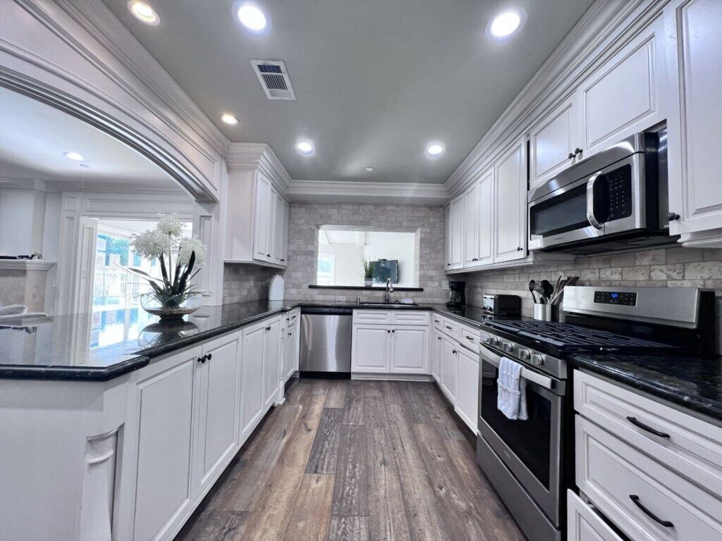 A modern kitchen with white cabinetry, a granite countertop, stainless steel appliances, and a view to the outside.
