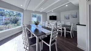 A dining area with a long table, white chairs, a flat-screen TV, and a view of the outdoors. - Sensational 6 Bedroom 4 Bathroom Pool Home (3 Master Bedrooms W/bathrooms) (Anaheim)