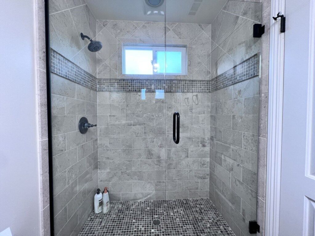 A walk-in shower with a tiled floor, a showerhead, a window, and a door.