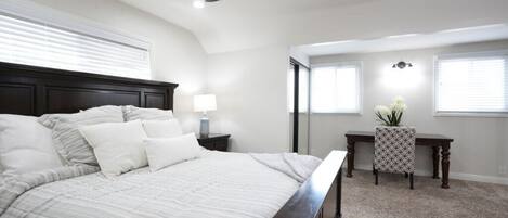 A bedroom with a bed, a ceiling fan, a nightstand, a desk, and a chair.