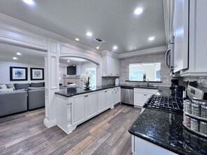 A modern kitchen with white cabinetry, a black granite countertop, and a stainless steel range hood.
