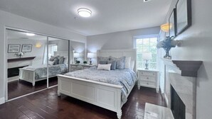 A bedroom with a large bed, a fireplace, a mirror, and a window. - Fantastic 5 Bedroom 4 Bath Home With new Pool & Jacuzzi (Anaheim)